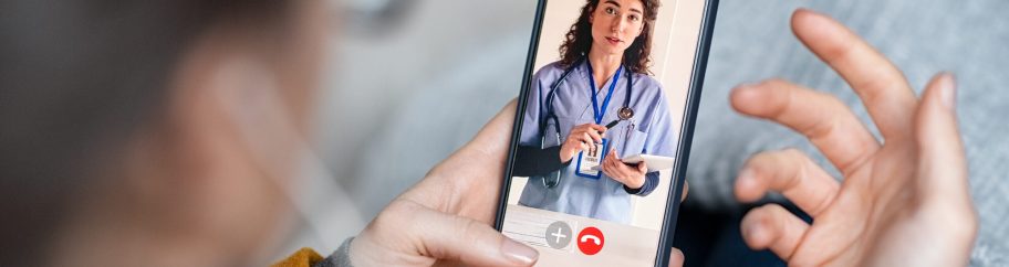 Close up of female doctor on video call with patient using smartphone. Rear view of young woman patient in conversation with specialist over video conferencing using smart phone. Sick woman patient lying on sofa doing video consultation with doctor using phone and explain her symptoms.